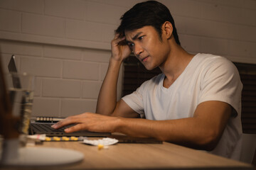 Stressed young Asian man on a desk looking at a laptop computer in darkness late at night, working,...