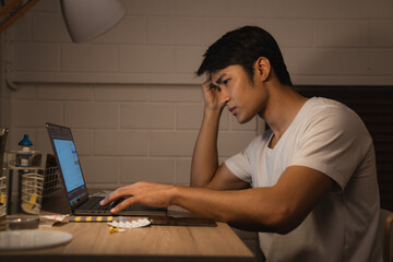 Stressed young Asian man on a desk looking at a laptop computer in darkness late at night, working, feeling serious thinking and determination at home in hard work or hard work.