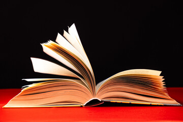 Pages of a thick book are turned on a red and black background.
