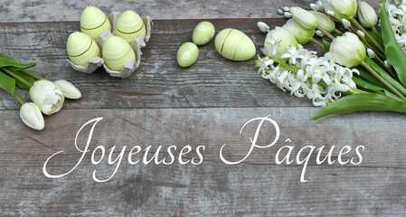 Arrangement floral avec des œufs de Pâques sur une planche de bois minable avec le texte Joyeuses...