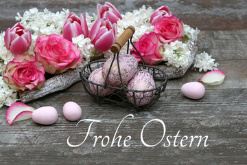 Blumen Arrangement mit  Ostereiern auf schäbigen Holzbrett mit dem Text Frohe Ostern.	