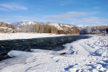 A frozen river bank with a distant mountain under a cloudy sky