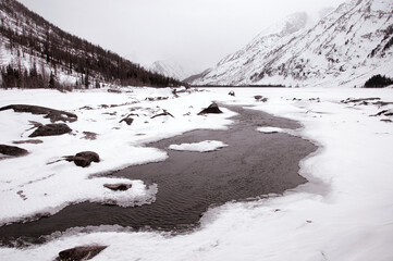 Freezing watercourse flows through snowy mountains and under polar ice cap
