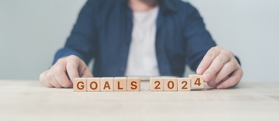 Person aligning wooden blocks spelling 'GOALS 2024', suitable for themes like New Year resolutions, future planning, or personal goal setting.
