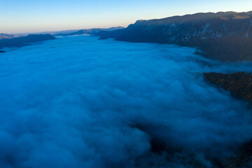 Fototapeta na wymiar Flying above the clouds in dawn. Misty morning in the valley, aerial view