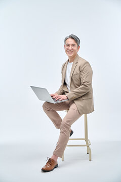 A middle-aged male teacher in a suit and glasses is sitting in a chair, holding a laptop, working with various expressions and poses.