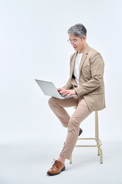 A middle-aged male teacher in a suit and glasses is sitting in a chair, holding a laptop, working with various expressions and poses.