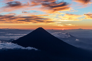 Silhouette of volcano de agua at firey orange sunrise seen from the top of volcano de acatenango, guatemala