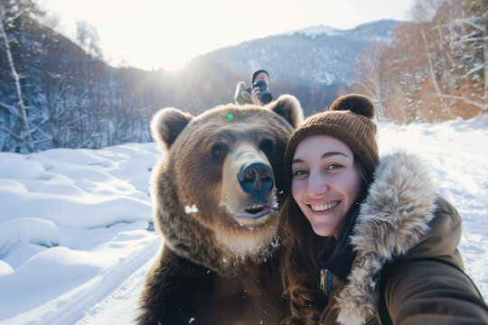A selfie of an attractive woman with brown hair and wearing winter , smiling at the camera while taking photos in front of her grizzly bear friend on snow mountain , unsplash photography style