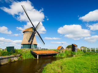 An old mill in the Netherlands. Historical building. A mill near a canal. Dutch architecture and history. Photo for postcard or background. - 766233760