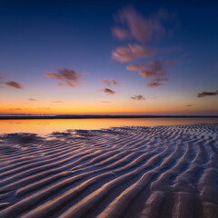 A seascape during sunset. Lines of sand on the seashore. Bright sky during sunset. A sandy beach at...