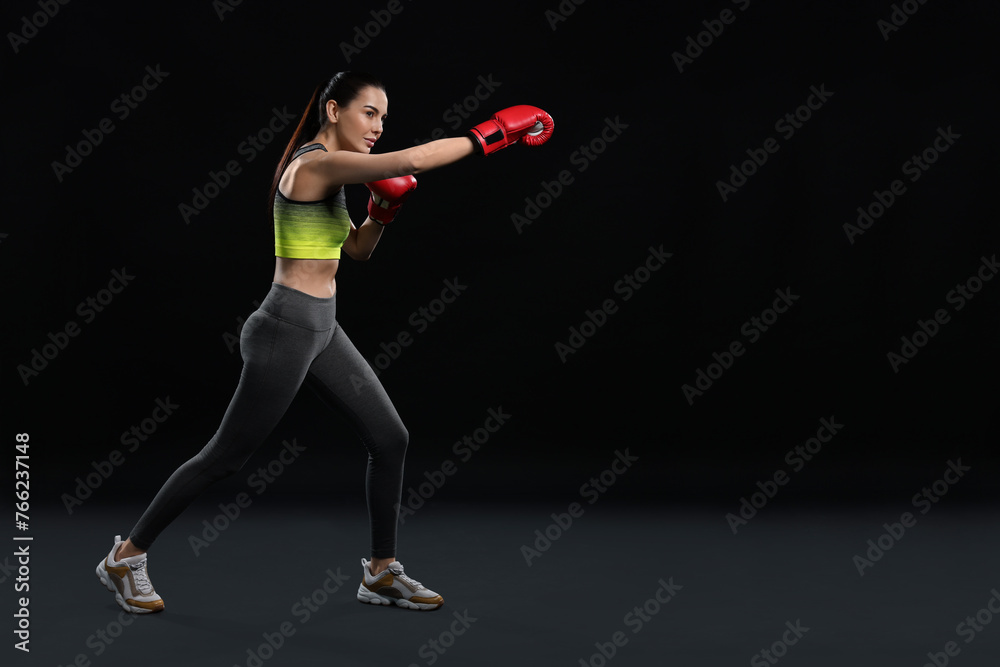 Poster Beautiful woman in boxing gloves training on black background. Space for text