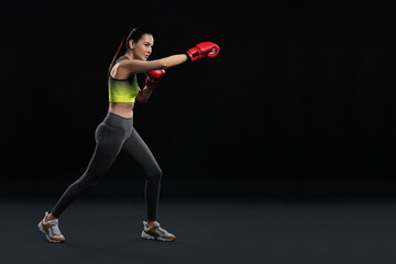 Fototapeta premium Beautiful woman in boxing gloves training on black background. Space for text