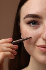 Beautiful woman drawing freckles with pen on brown background, closeup