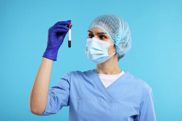 Laboratory testing. Doctor with blood sample in tube on light blue background