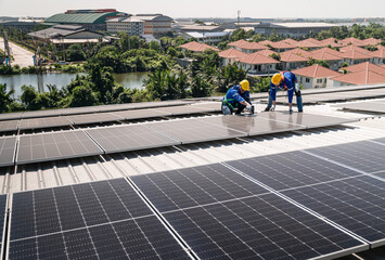 Male technician installing solar photovoltaic panels on factory roof. Worker in hardhat builds...