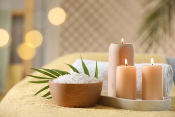 Spa composition. Burning candles, sea salt and towel on soft yellow surface