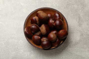 Obraz premium Roasted edible sweet chestnuts in bowl on light grey table, top view