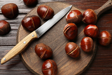 Roasted edible sweet chestnuts and knife on wooden table, flat lay