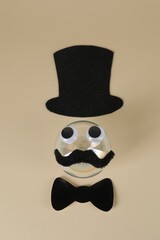 Man's face made of fake mustache, ball, hat, bow tie and eyes on beige background, top view