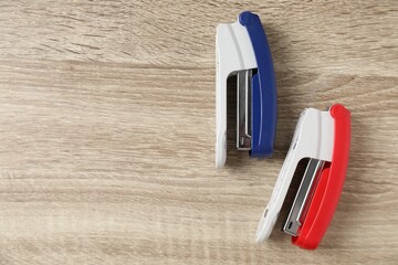 Color staplers on wooden table, flat lay. Space for text