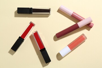 Different lip glosses on pale yellow background, flat lay