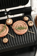 Electric grill with homemade sausages, rosemary and mushrooms on table, above view
