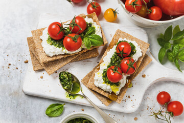 Wholegrain crackers with cottage cheese, pesto and cherry tomatoes high angle view