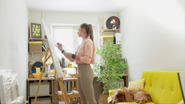 Young woman artist drawing picture on canvas using acrylic paints. Talented female artist working on painting of sea and mountains. Female artist works at home. Drawing process. Hobby. 4K, UHD