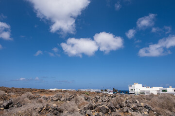 Deserted landscape on the outskirts of the village of Arrieta. Dry bushes, red earth and mountains in the background. Large white clouds. Village of Arrieta. Lanzarote, Canary Islands, Spain