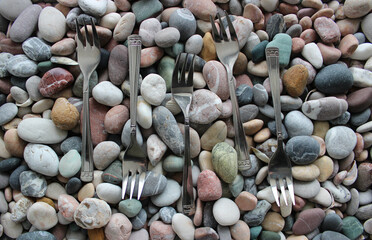 Identical Silvery Dessert Forks Laid Out In A Row On Colored Sea Stones
