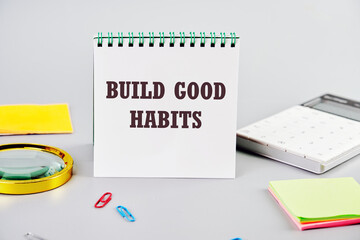 BUILD GOOD HABITS motivational concept text on a white notepad on a gray background next to office supplies