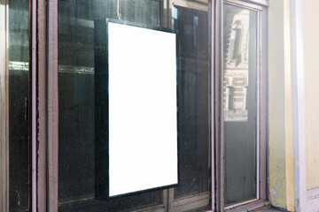 Vertical blank advertisement board on dusty storefront window in urban setting. Reflective glass surface shows city life, ideal for marketing mockup and urban design presentation