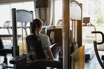 Asian sport woman working out a weight machine for legs at gym fitness. The machine is a multi-station weight machine. The woman is lifting weights and focused on her workout. - obrazy, fototapety, plakaty