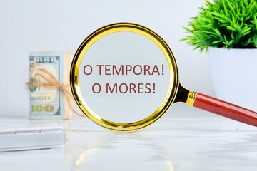 o tempora, o mores (O, the times O, the morals) Latin phrase through a magnifying glass on a gray background, a roll of banknotes and a green plant in the background - obrazy, fototapety, plakaty