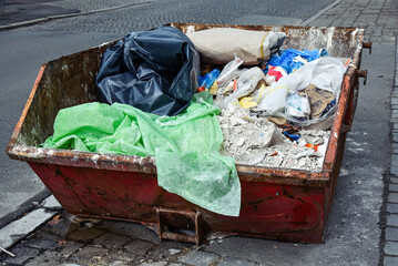 Metal container is filled with construction waste on the street.