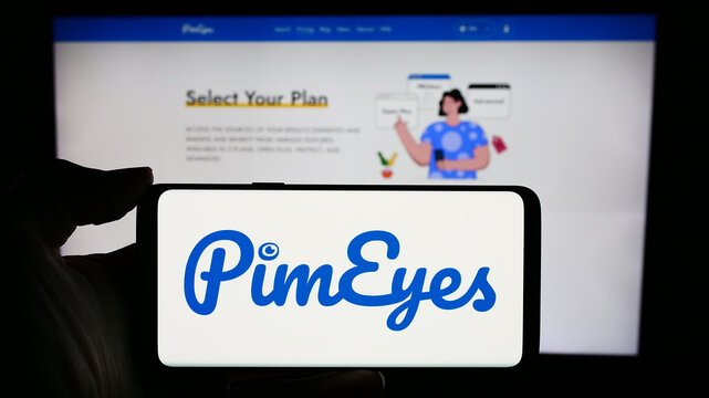 Stuttgart, Germany - 03-13-2024: Person holding cellphone with logo of facial recognition search company PimEyes in front of business webpage. Focus on phone display.