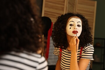 Young woman applying mime makeup near mirror indoors