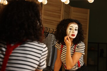 Young woman applying mime makeup near mirror indoors