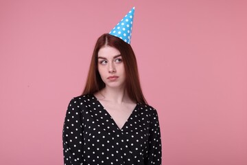 Sad woman in party hat on pink background