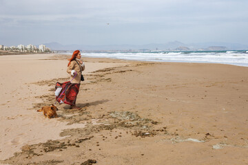 Mujer paseando a la perrita Nami mientras lucha con el fuerte viento en la playa de el Altet,...