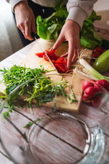 A close up of girl's or woman's hands peeling and cutting vegetables with knife making salad	