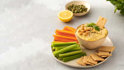 A dish of hummus with a side of carrots, celery and more hummus on a plate. Copy space