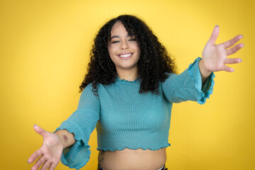 African american woman wearing casual sweater over yellow background looking at the camera smiling with open arms for hug
