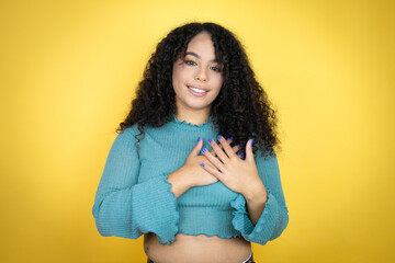 African american woman wearing casual sweater over yellow background smiling with her hands on her...