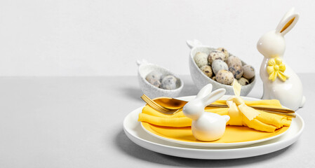 White yellow plates, eggs in figured bowls, golden cutlery, ceramic bunnies on neutral. Copy space.