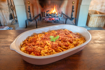 pan with typical Italian tagliatelle with tomato sauce on a wooden table against the backdrop of a burning fireplace in a country house 
