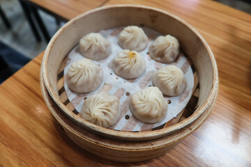 Fototapeta na wymiar close up of Taiwanese Chinese steamed meat soup dumplings in a bamboo caged container on a wooden table