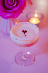 close up of a pink cocktail on a table with candles and roses