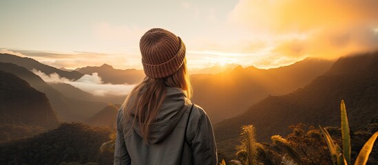 A thoughtful woman standing on the mountain top, staring at the captivating sunset view with the mountains in the background - obrazy, fototapety, plakaty